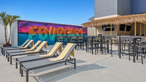 Un espace de détente sur le toit, avec des fauteuils et des tables, une fresque murale sur laquelle on peut lire le mot « FLOURCAST », et une structure avec un toit de chaume.