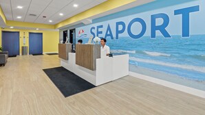 Un espace d’accueil avec une grande enseigne indiquant « SEAPORT », un comptoir d’accueil en bois et une vue sur l’océan par une fenêtre.