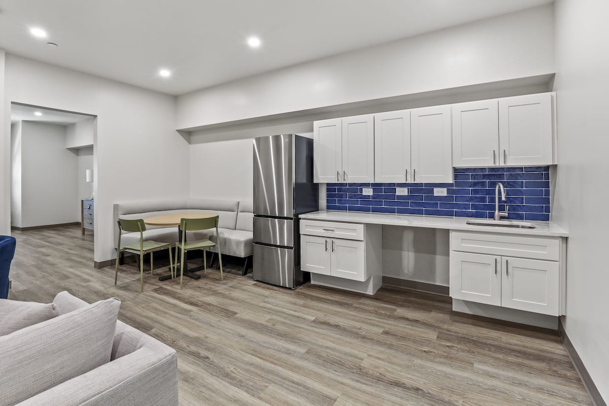 A modern kitchen with white cabinets, a stainless steel refrigerator, and a blue-tiled backsplash.