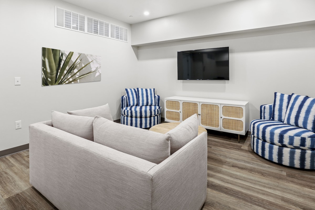 A modern living room with a sofa, two striped armchairs, a television, and a decorative wall piece.