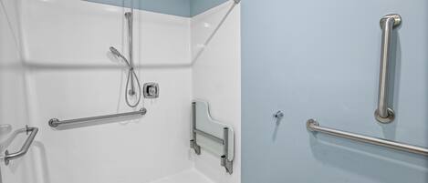 Un área de ducha con barra de apoyo, cabezal de ducha de mano y grifo empotrado en la pared.