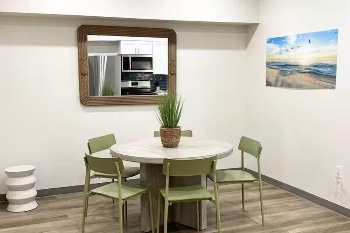 A modern dining area with a round table, four chairs, a potted plant, and a wall-mounted mirror.