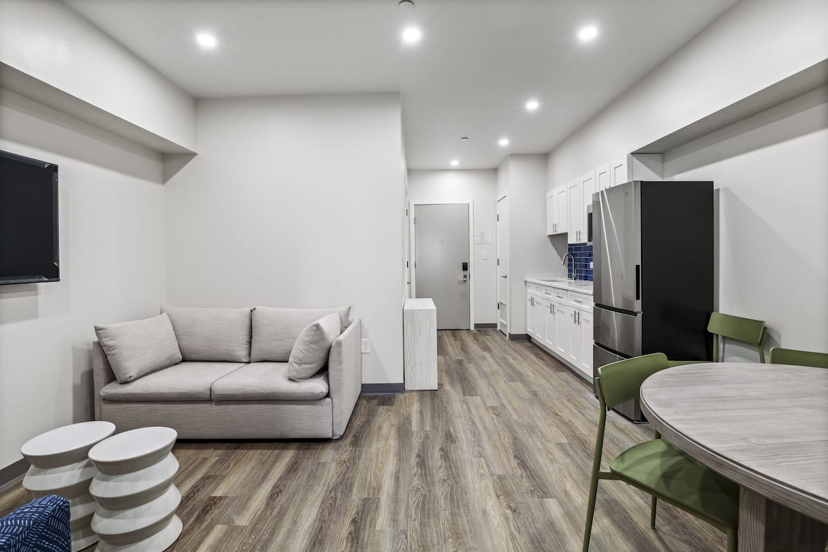 A modern kitchen with white cabinets, a black refrigerator, and a wooden floor.
