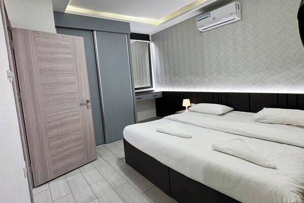 A modern bedroom with a bed, bedside tables, a wardrobe, and an air conditioning unit.