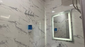 Ein Badezimmer mit Marmorwand, Waschbecken, Spiegel, Duschkopf und Mülleimer.