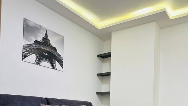 A modern living room with a dark grey sofa, a glass coffee table, and a framed picture of the Eiffel Tower on the wall.