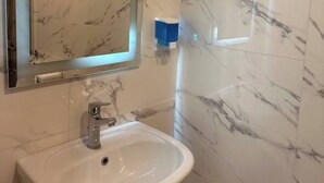 A bathroom with a marble sink, a mirror, and a towel dispenser.
