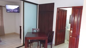 A dining area with a table and chairs, a television mounted on the wall, and a sliding door leading to a bathroom. - Marina Loft Condo #214 (Sardinal)
