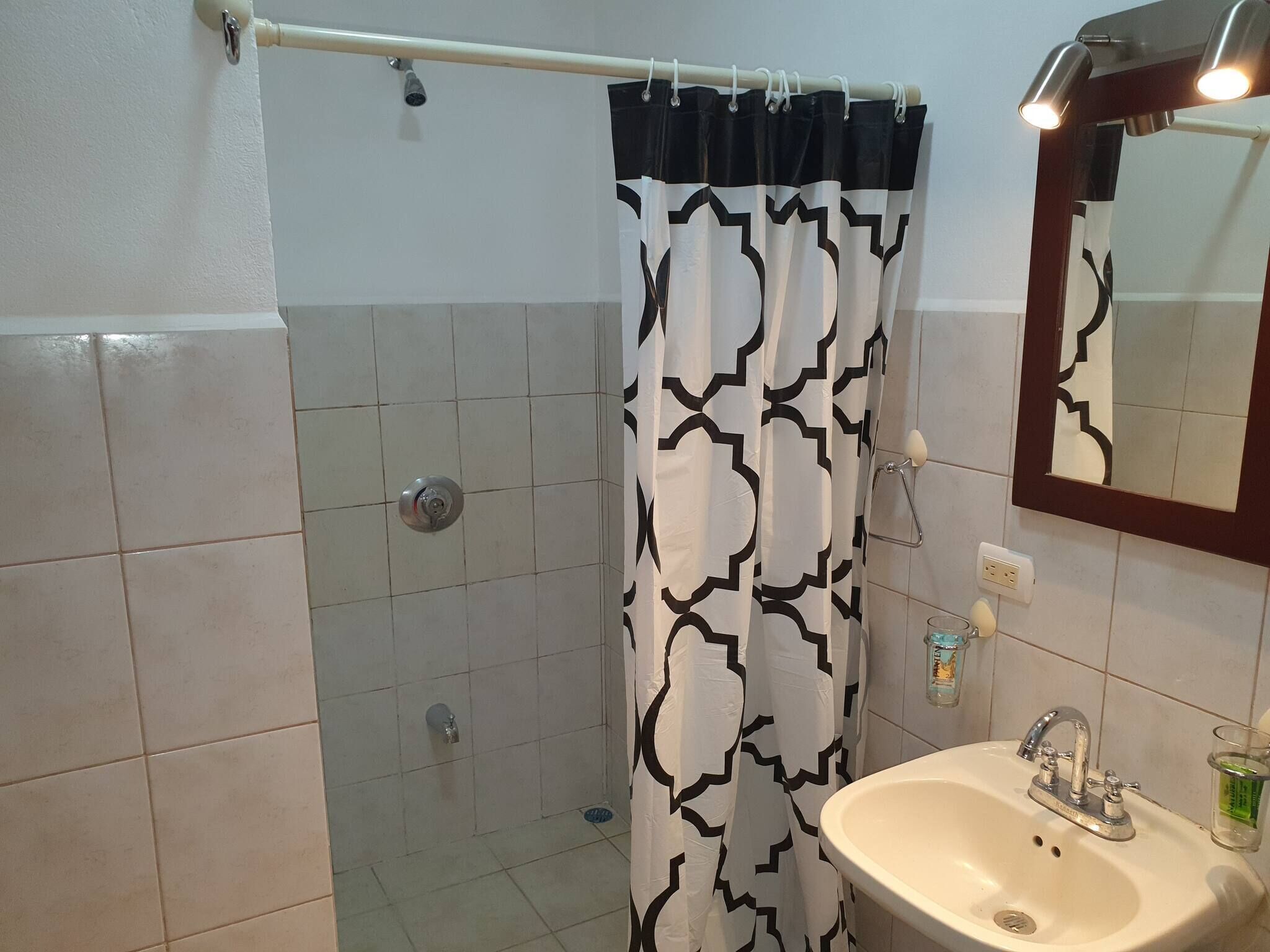 A bathroom with a shower, a sink, a mirror, and a towel rack.