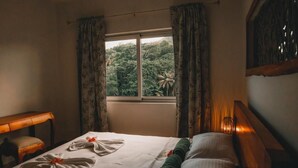 A hotel room with a bed, a desk, and a window with curtains. - Kannel Apartments Seychelles - 2 Bedroom (Mahé Island)