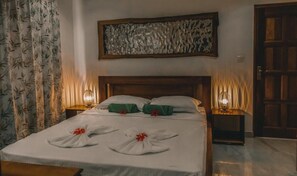 Un lit bien fait, agrémenté de serviettes et d’un ruban rouge, une tête de lit en bois, une œuvre d’art murale et deux lampes de chevet.