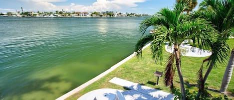 A waterfront property with a pool, palm trees, and a view of the water.