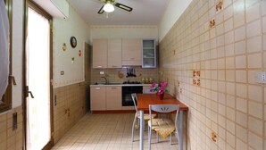 Cocina compacta con comedor, que incluye un ventilador de techo, paredes con azulejos y una pequeña mesa con sillas.