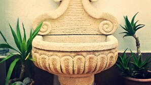Una fuente de piedra con un adorno superior, flanqueada por dos plantas en macetas.