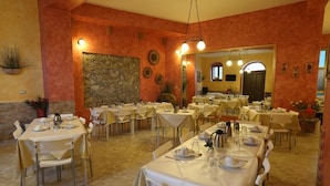 Comedor con varias mesas dispuestas para el servicio, paredes de piedra y un espejo grande que refleja la estancia.