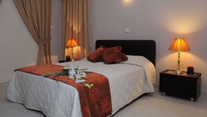 Un lit bien fait, recouvert d’une couvre-lit à motifs rouges et blancs, avec deux lampes de chevet et une table de chevet sur laquelle se trouve une lampe.
