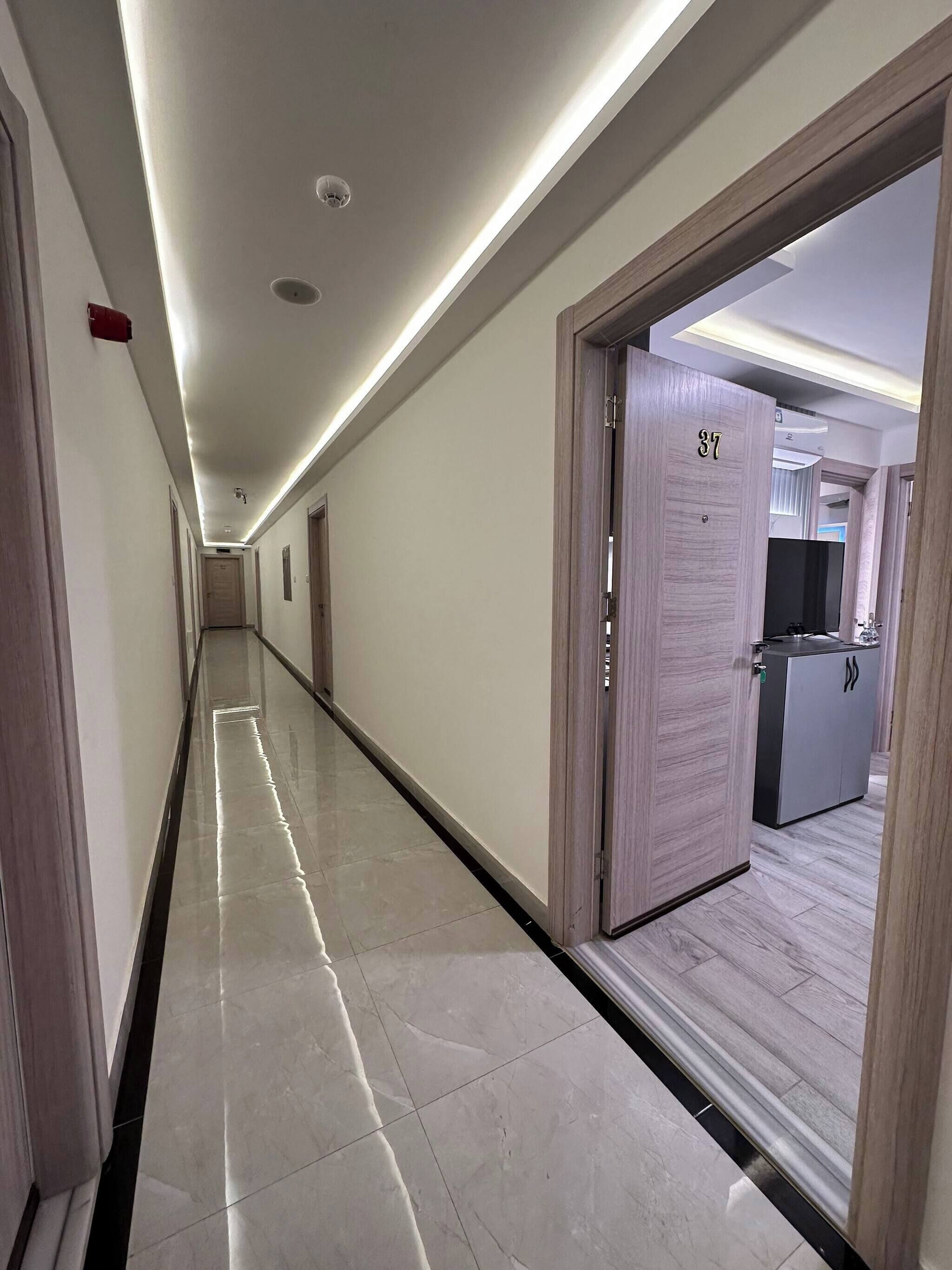Un couloir d’hôtel, long et bordé de portes, avec un espace d’accueil.