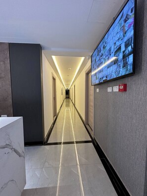 A hotel hallway with a long corridor, a reception desk, and a security camera.