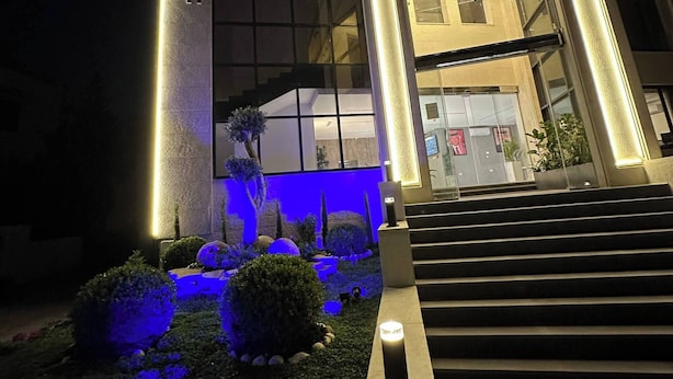 A modern building with illuminated vertical lines, a visible entrance, and a well-lit garden area. - Privet Apartment 37 for Three Near Downtown Kh&sh (Amman)