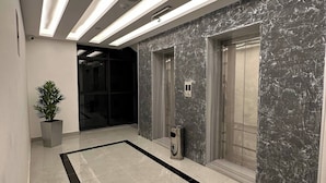 A modern lobby with a marble wall, a potted plant, and a trash can. - Privet Apartment 37 for Three Near Downtown Kh&sh (Amman)