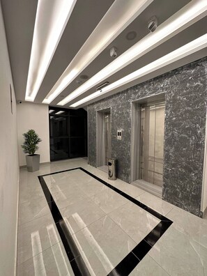 A modern lobby with a marble wall, a potted plant, and a trash can. - Privet Apartment 37 for Three Near Downtown Kh&sh (Amman)
