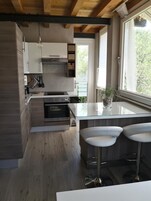 Eine moderne Küche mit Holzausstattung, einem Einbauofen, einer großen Kochinsel mit Barhocker und einem Fenster mit Blick auf Grünflächen.