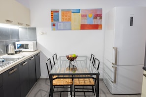Cocina compacta con microondas, pileta y heladera. Hay una mesa de comedor con sillas y un cuenco de fruta encima.