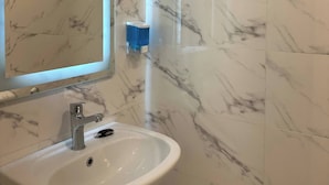 Ein Badezimmer mit weißem Waschbecken, einem Spiegel und Wänden mit Marmoroptik.