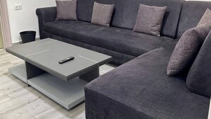 Ein modernes Wohnzimmer mit einem grauen Ecksofa, einem grauen Couchtisch und einer Fernbedienung auf dem Tisch.