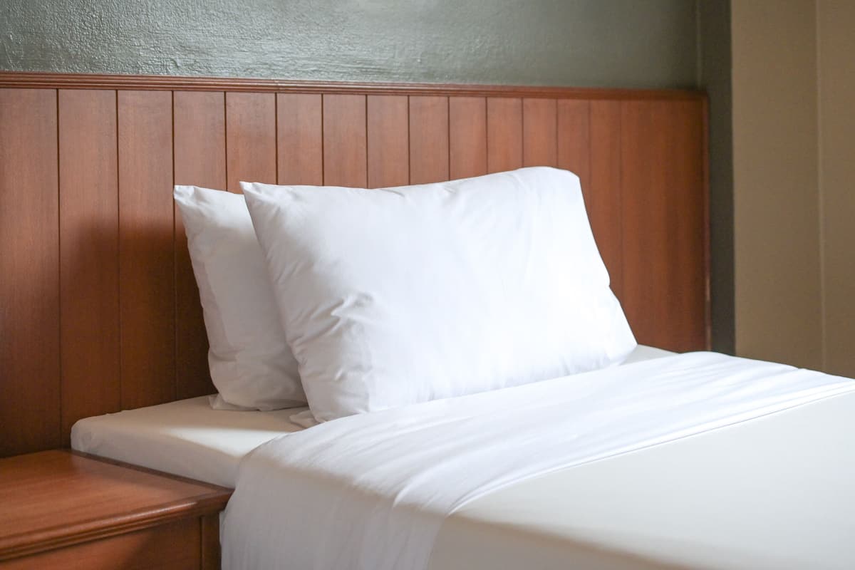 A neatly made bed with white linens and pillows, a wooden headboard, and a wooden nightstand.