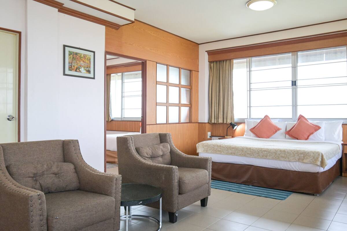 A hotel room with a bed, two armchairs, a small table, and a window with curtains.