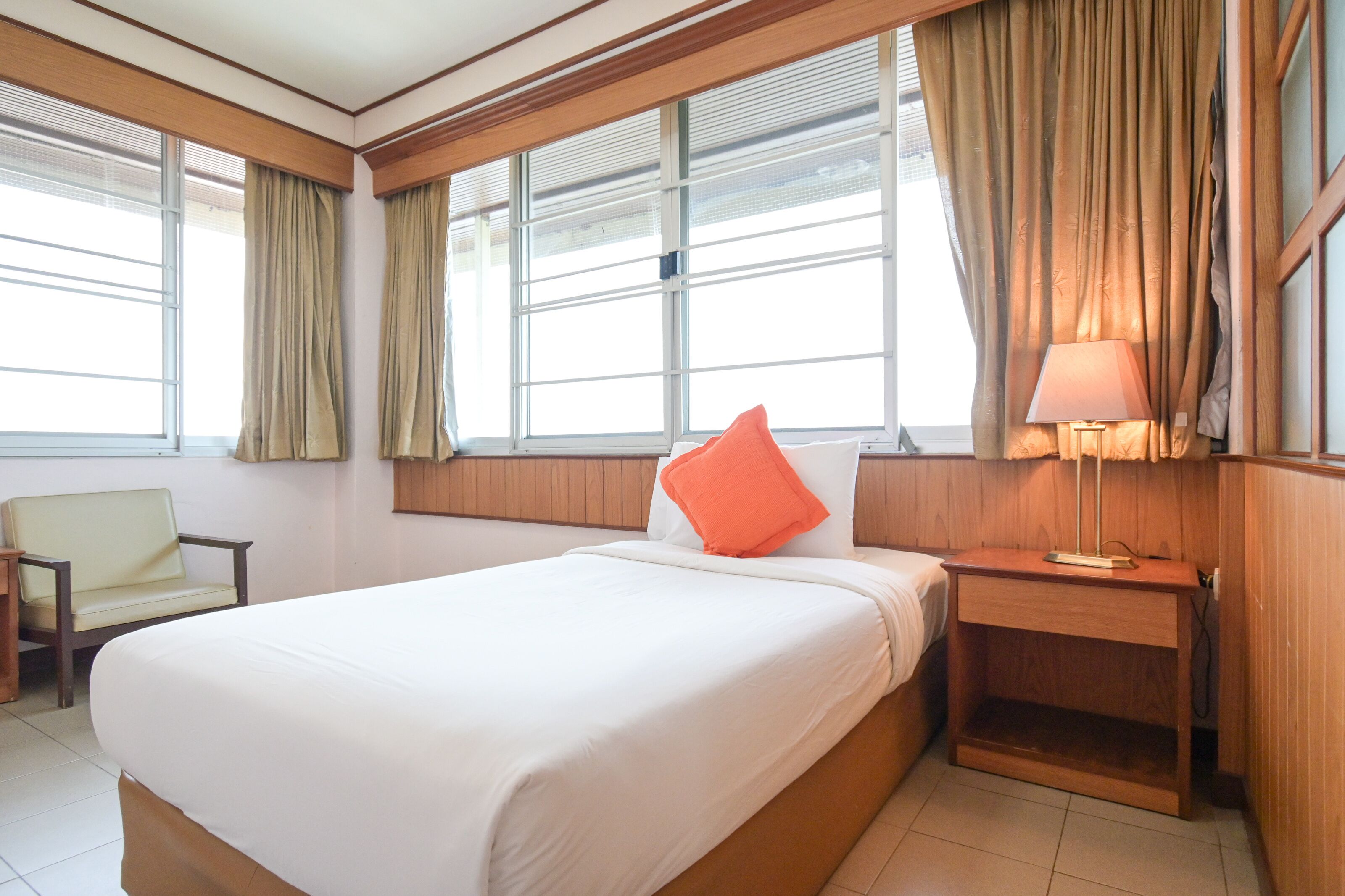 A hotel room with a large bed, a bedside table with a lamp, a chair, and a window with curtains.