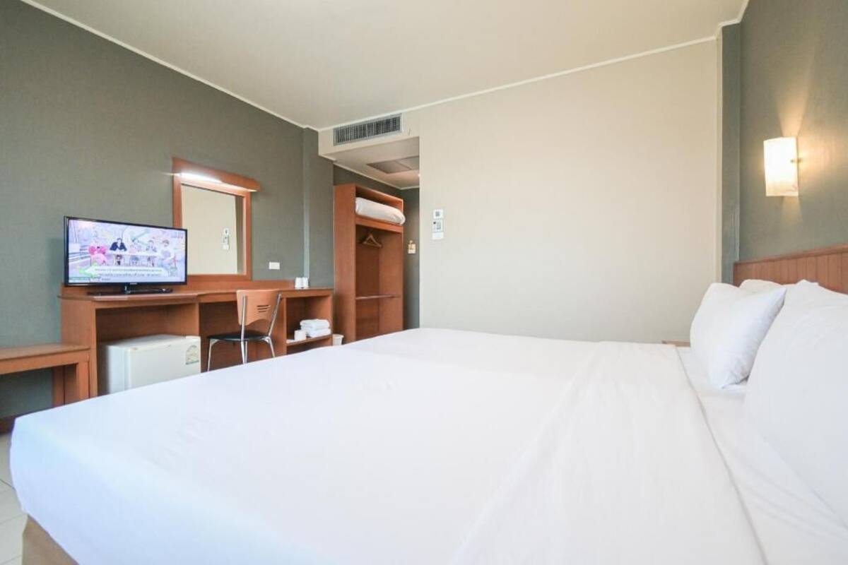 A hotel room with a bed, a desk with a computer, a chair, a TV, a wardrobe, and a mirror.