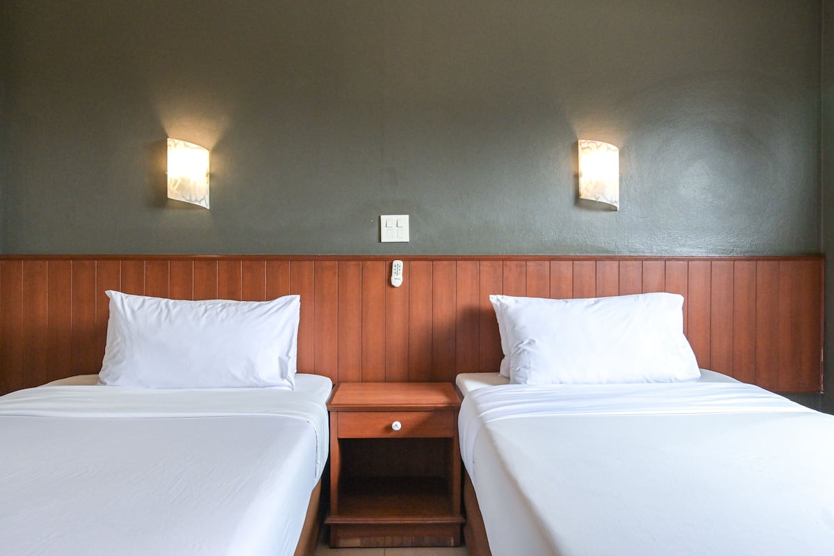 A hotel room with two single beds, wooden headboard, and two wall-mounted light fixtures.