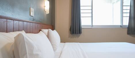 A hotel room with a bed, a headboard, a wall-mounted light, and a window with curtains.