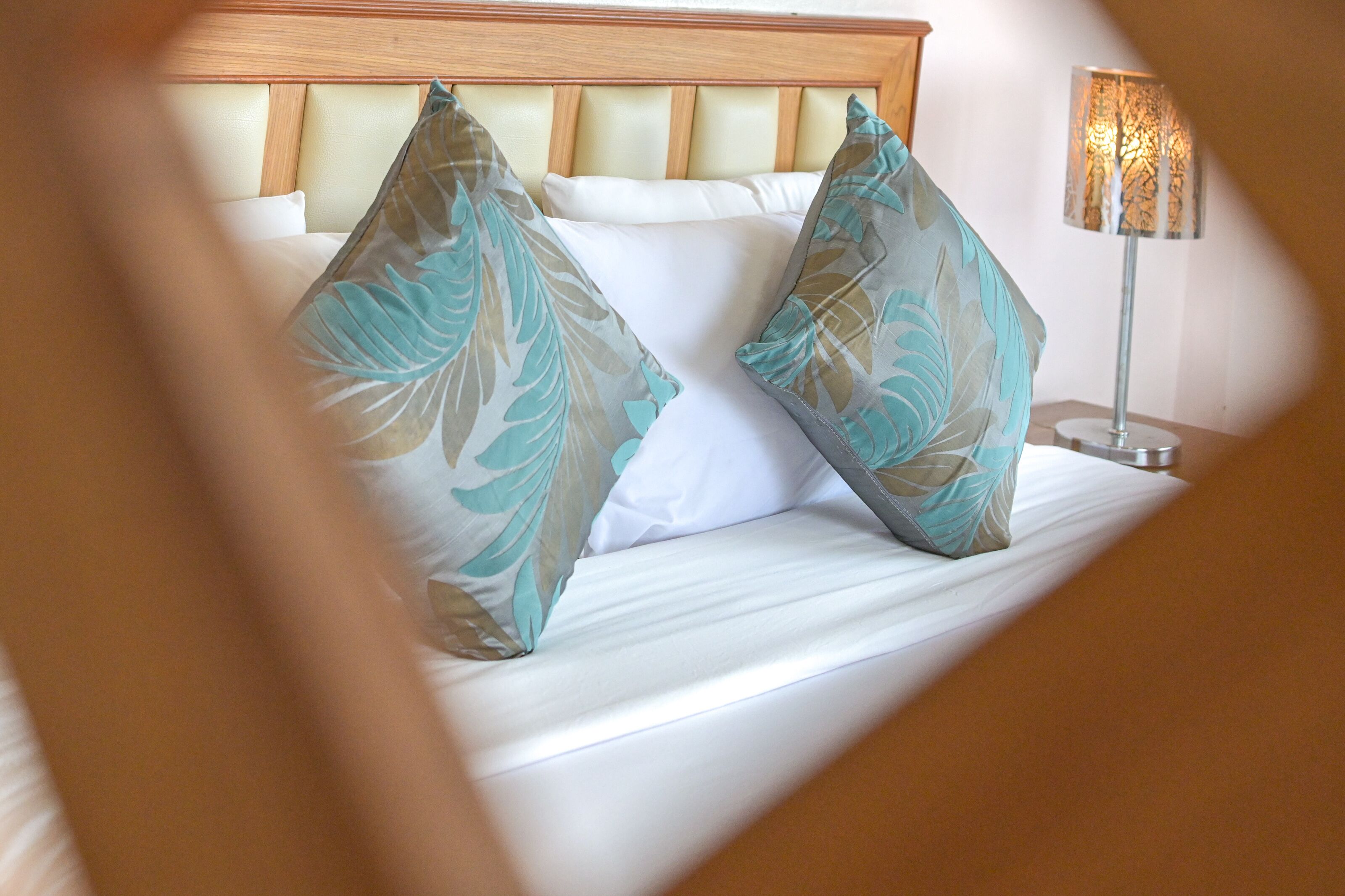 A bed with a headboard, two pillows with a leaf pattern, and a bedside lamp.