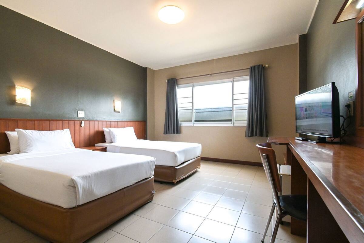 A hotel room with two beds, a television, a desk, and a window with curtains.