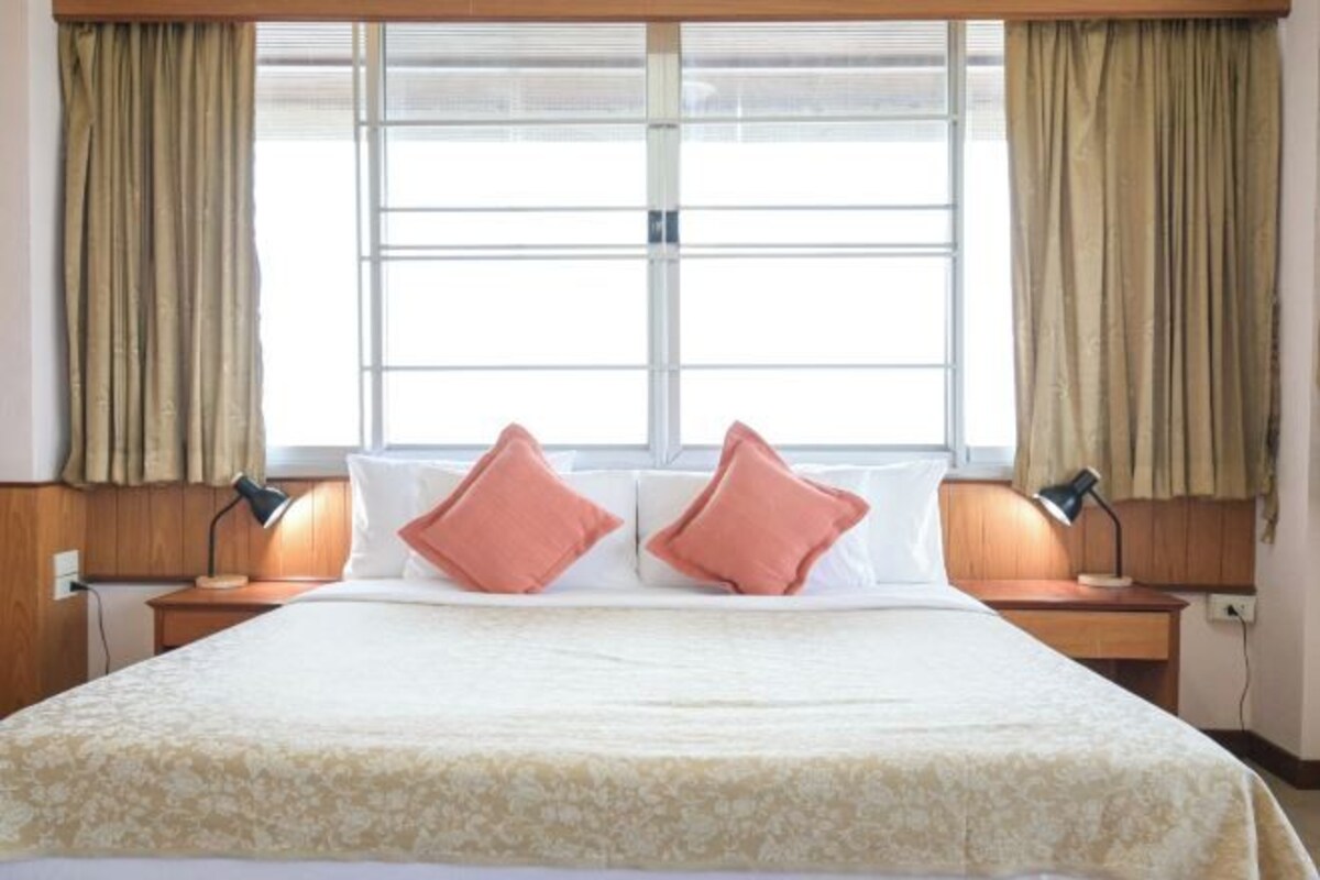 A hotel room with a large bed, two bedside lamps, and a window with curtains.