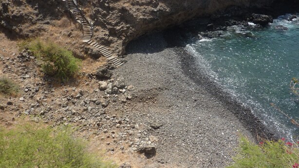 Una playa rocosa con una escalera que baja hacia el agua.