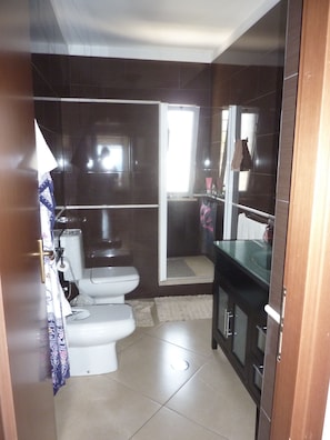 Casa de banho com sanita, cabine de duche em vidro e lavatório.