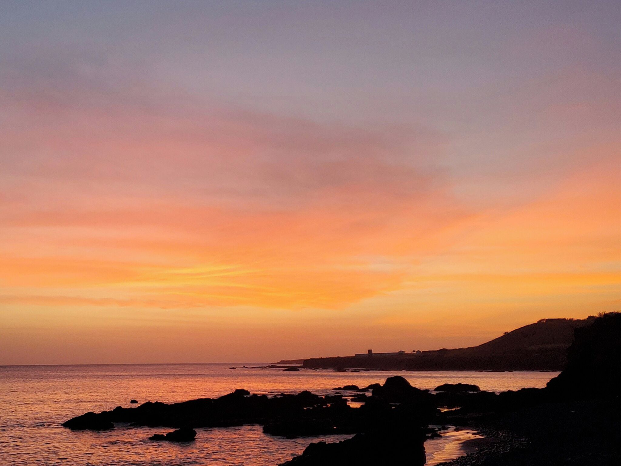 Atardecer costero con afloramientos rocosos y una línea de costa distante.