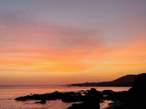 Um pôr do sol costeiro com rochedos e a linha do horizonte distante.