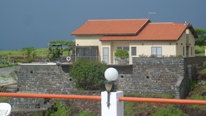 Una casa costera con tejado rojo de baldosas, pared de piedra y vista al mar.