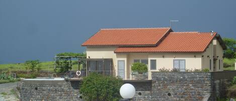 A coastal house with a red-tiled roof, a stone wall, and a view of the sea.