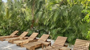 Wooden lounge chairs and benches arranged outdoors, surrounded by dense green foliage.