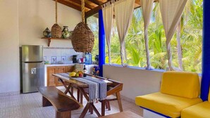 A kitchen with a refrigerator, wooden table, benches, and a yellow sofa.