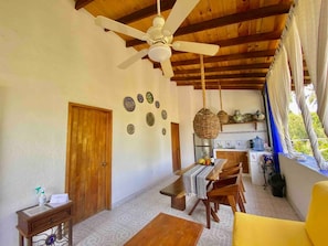 A dining area with a wooden table and chairs, a ceiling fan, and a view of the kitchen through an open door. - Villa Palomas A Unos Pasos De Playa La Ropa (Zihuatanejo)