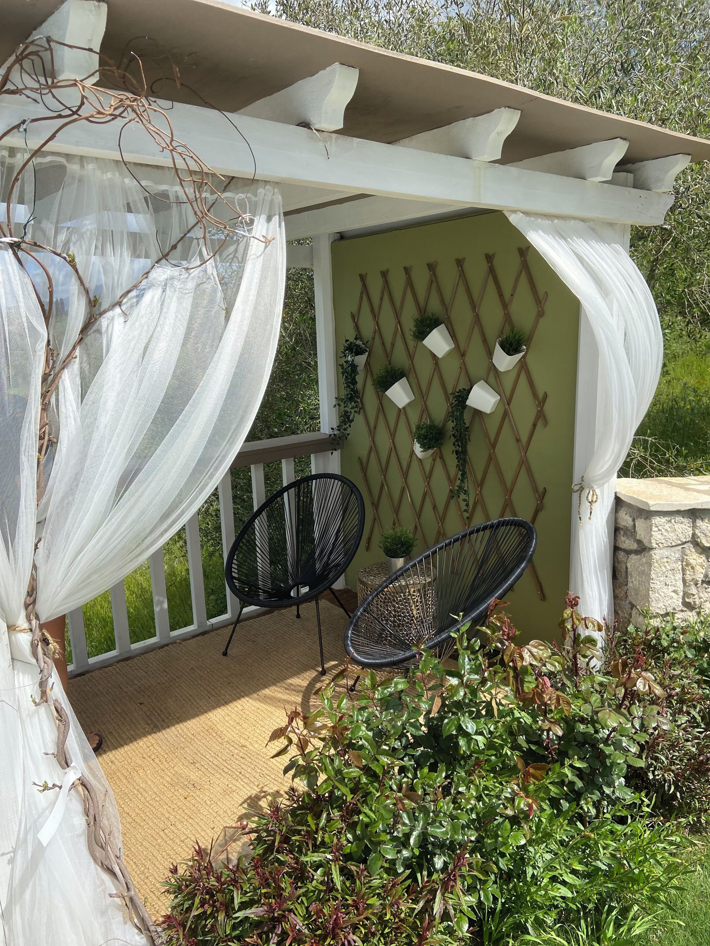 Un patio couvert agrémenté d’une pergola, de deux chaises et de plantes en pot.
