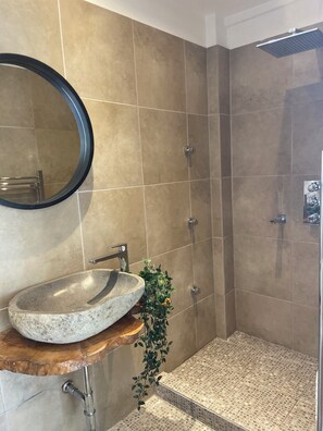Ein Badezimmer mit einem SteinklopfZuber, einem Spiegel, einer Dusche und gefliesten Wänden.