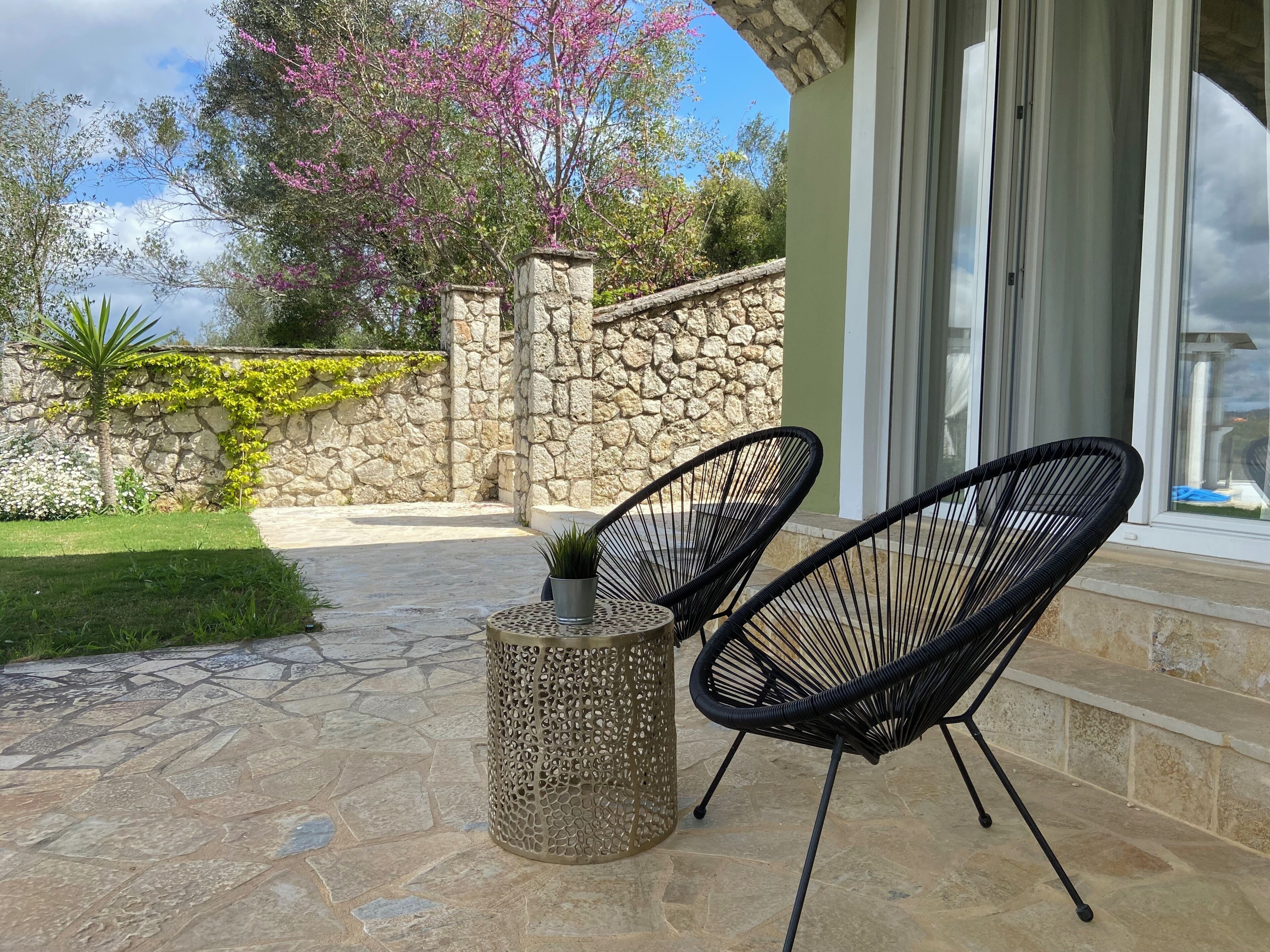 A patio with stone flooring, two black chairs, a metal table, and a potted plant.